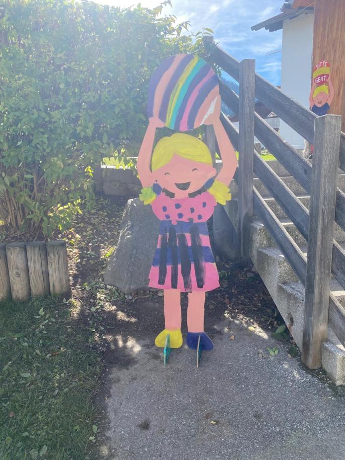 Auf dem Bild sieht man ein Mädchen aus Holz, dass einen bunten Ball trägt